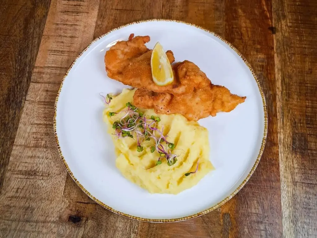 Paniertes Hähnchenschnitzel serviert mit Kartoffelpüree und Zitrone