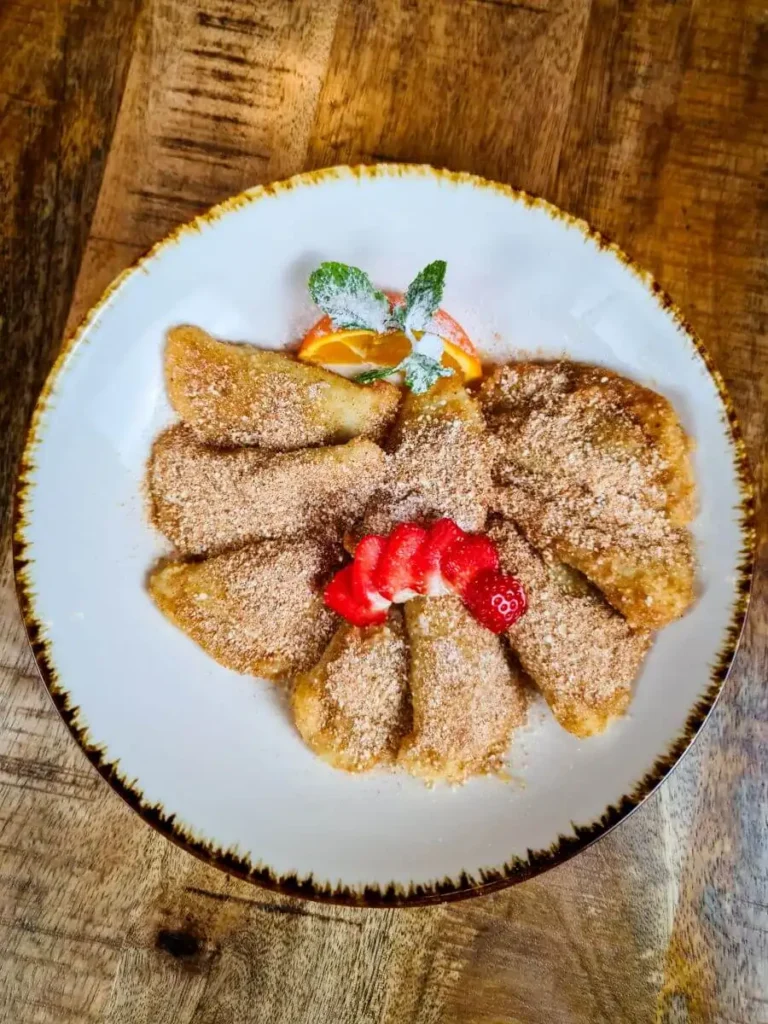 Hausgemachte Pflaumen-Piroggen mit Zucker bestäubt und mit Obst serviert